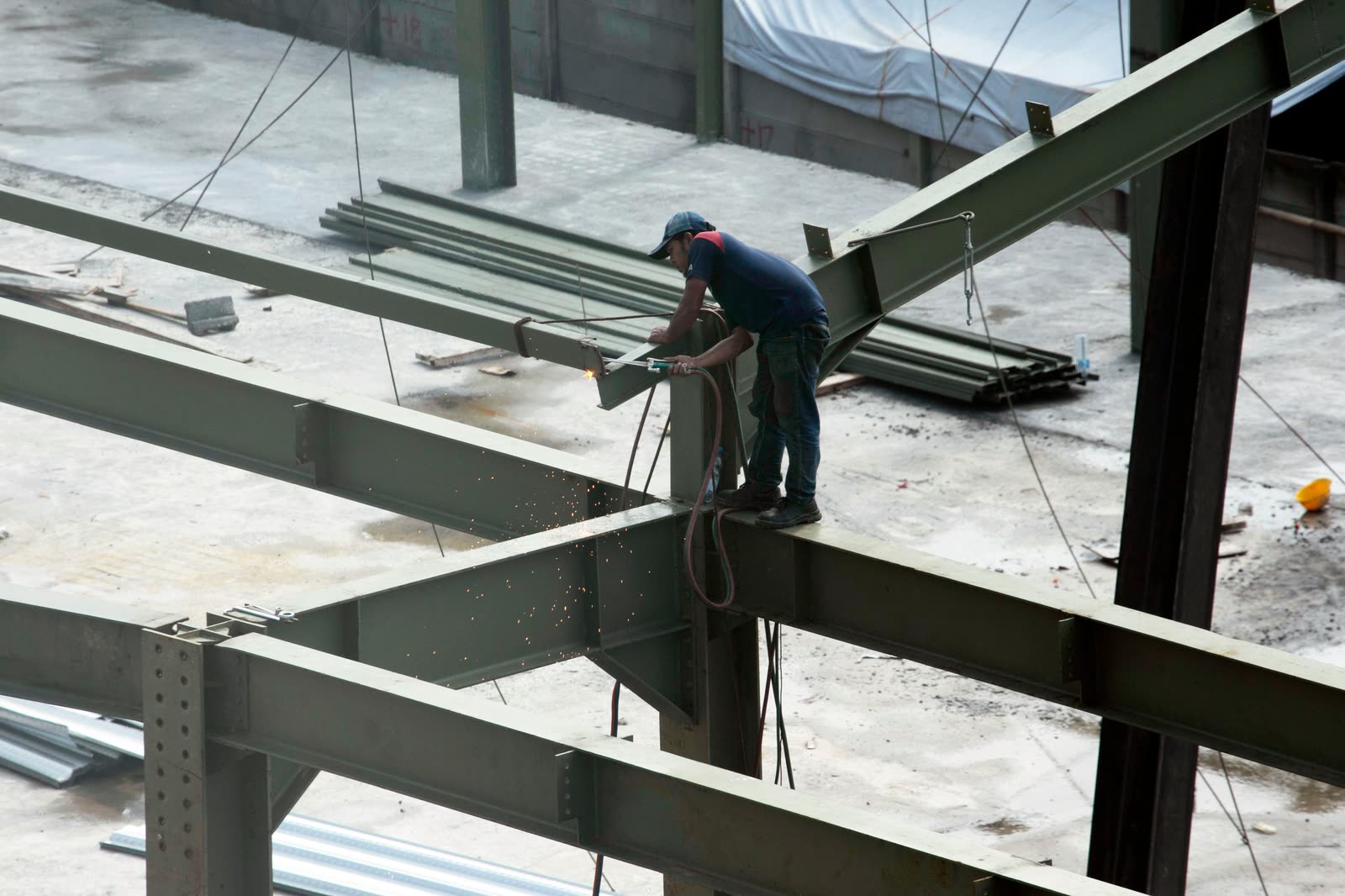 A worker welding steel beams on an upper floor of a structure.