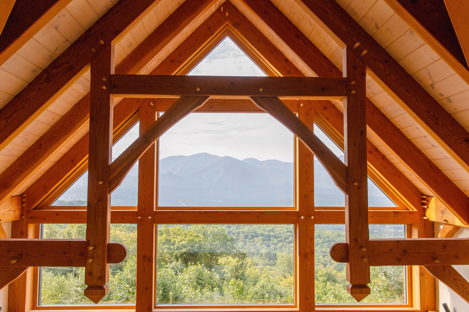 A timber-framed interior with tall windows looking out to forest and mountains.